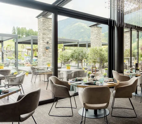 Restaurant in der Golf Lodge mit runden gedeckten Tischen und moderne Kristalle an der Decke vor Panoramafenstern