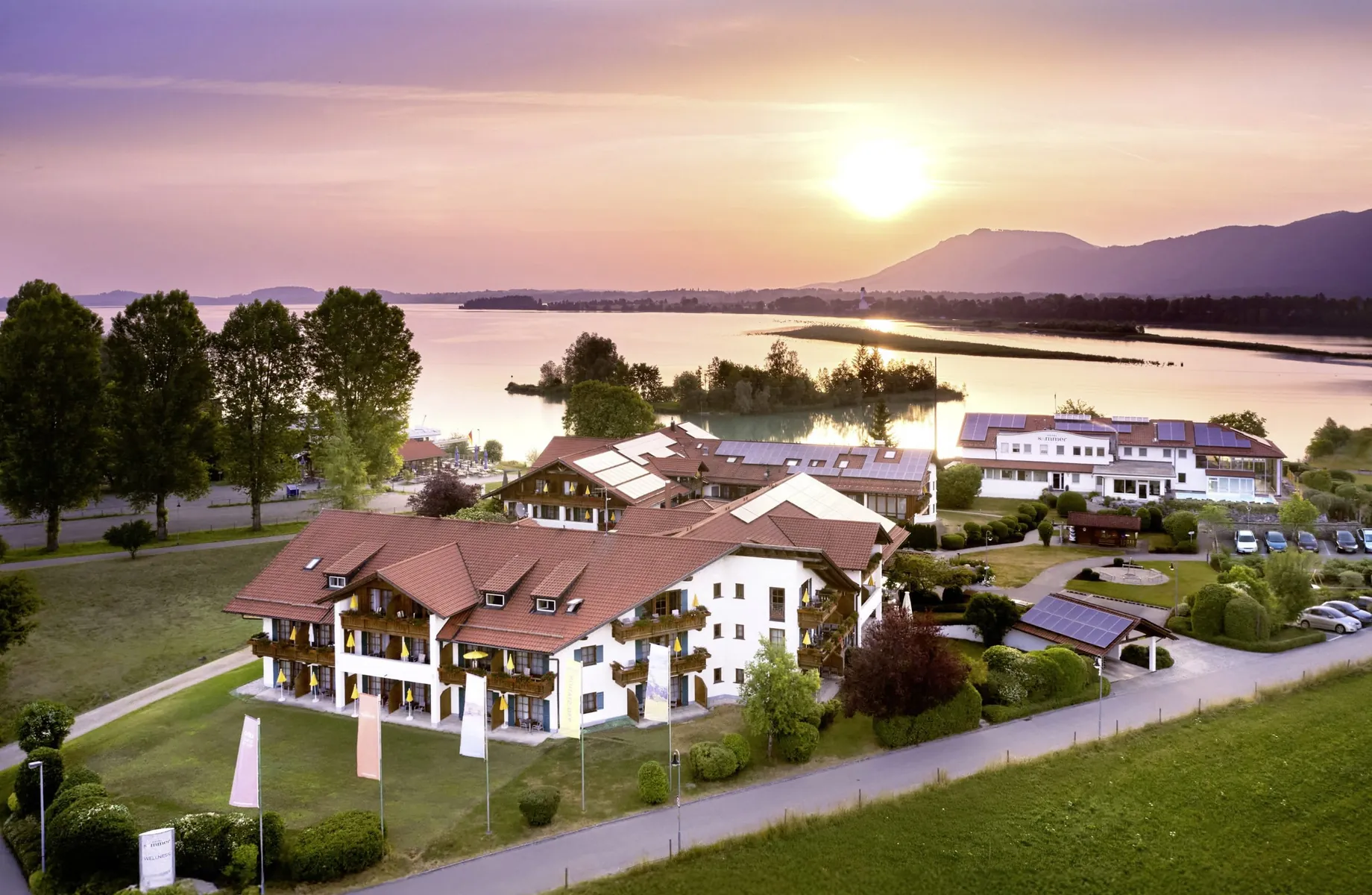 Luftaufnahme des Hotel Sommer in Füssen mit Forggensee im Hintergrund und rosa-orange untergehender Sonne