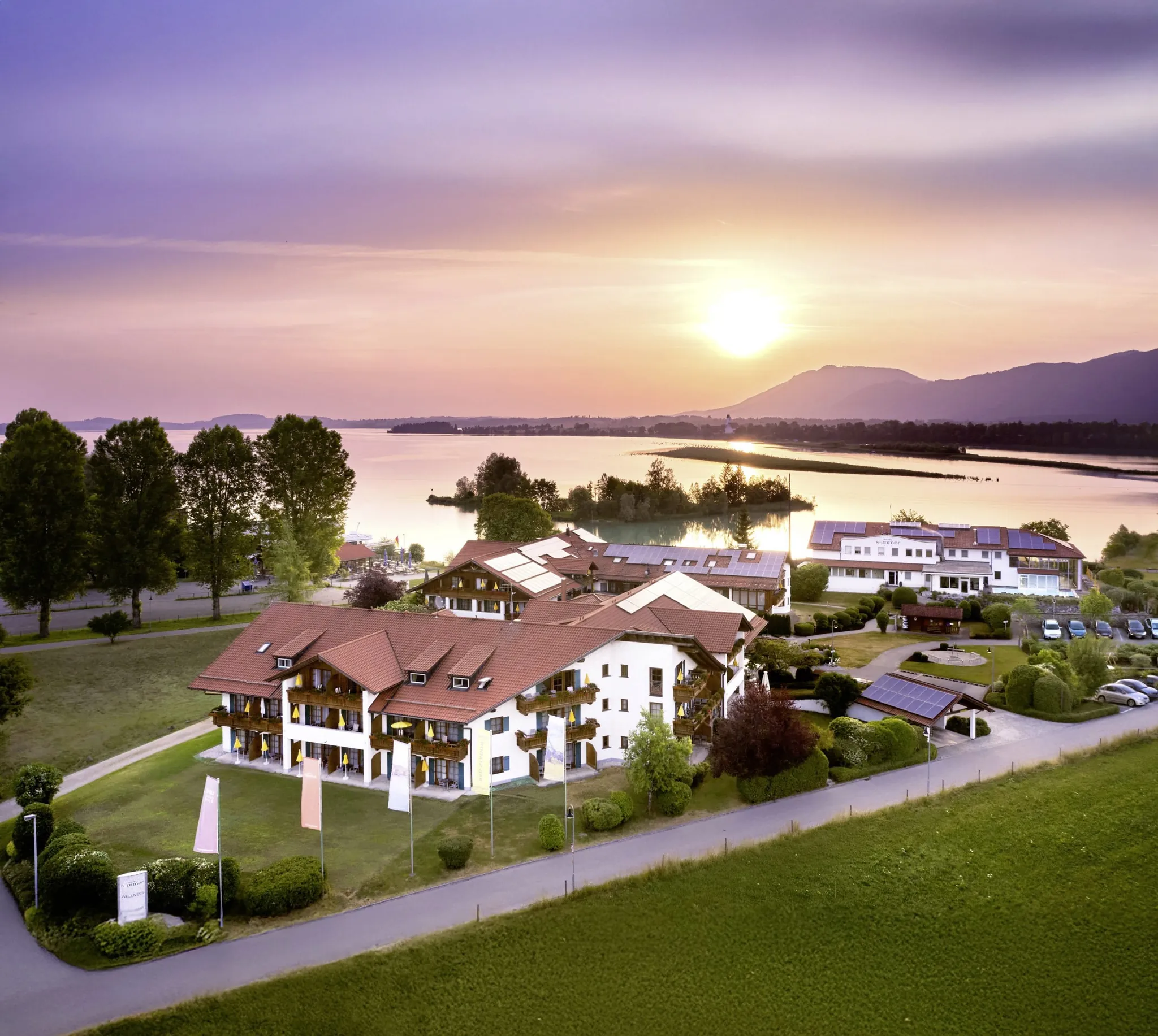Luftaufnahme des Hotel Sommer in Füssen mit Forggensee im Hintergrund und rosa-orange untergehender Sonne