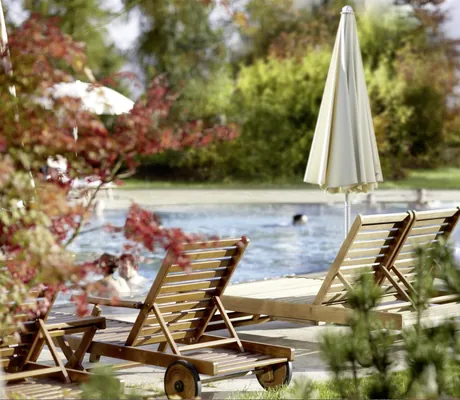 Holzliegen und weiße Sonnenschirme am Beckenrand des Außenpools des Interalpen-Hotel Tyrol