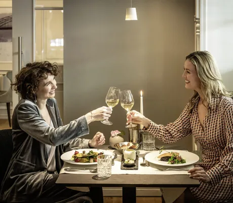 zwei Frauen sitzen am gedeckten Dinnertisch im Moselschlösschen Spa & Resort und prosten sich zu