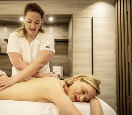 blonde Frau wird im Moselschlösschen Spa & Resort von dunkelhaariger Therapeutin auf der Liege massiert