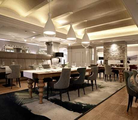 Restaurant im Moselschlösschen Spa & Resort mit langem Holztisch und drei großen weißen Deckenleuchten