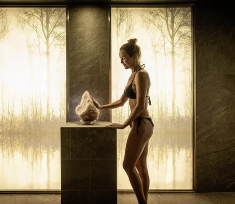 Frau in schwarzem Bikini berührt im Salzraum des Moselschlösschen Spa & Resort einen großen Salzstein