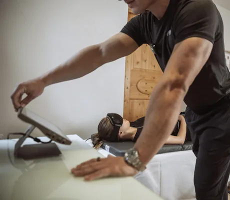 Mann schaut auf ein Tablet während Frau mit VR-Brille auf einer Liege liegt im Posthotel Achenkirch