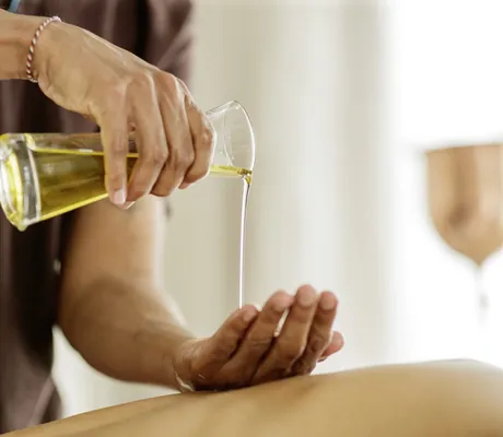 Masseur gießt aus Glaskaraffe Öl auf seine Hand im Posthotel Achenkirch