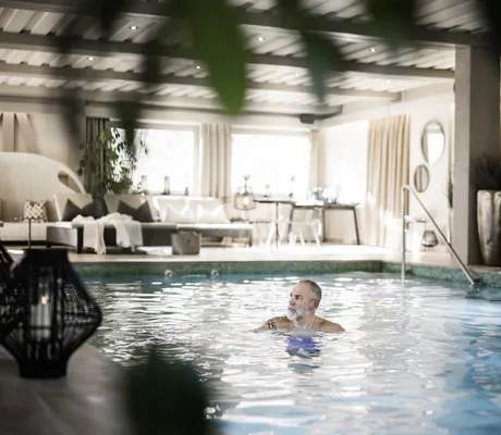 älterer Mann mit Tattoo schwimmt im Indoorpool des Romantik Hotel Stafler