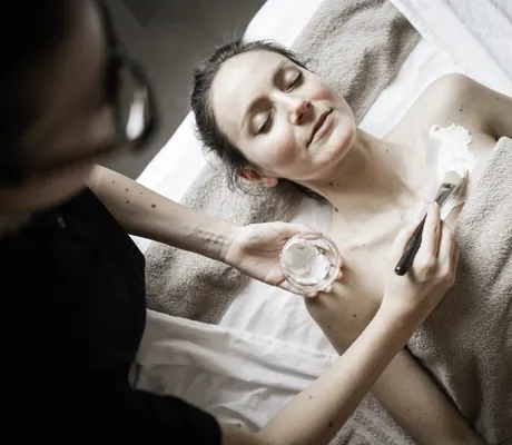 dunkelhaarige Frau wird von einer Therapeutin mit Creme eingepinselt im Romantik Hotel Stafler