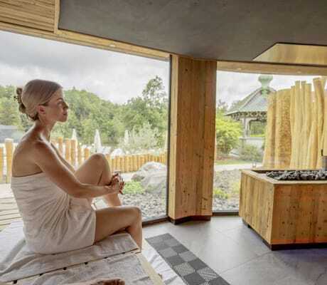 Frau eingehüllt in beiges Handtuch sitzt in der Sauna des Romantischer Winkel mit Blick auf Holzzaun