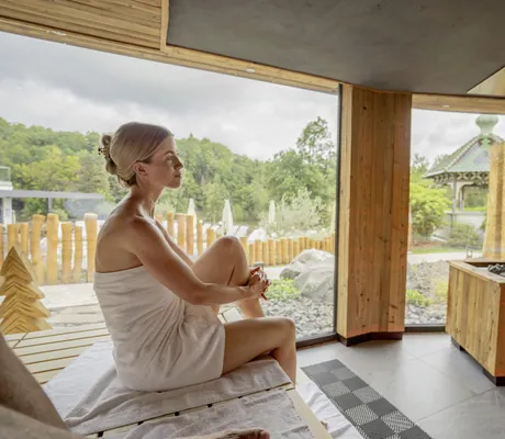 Frau eingehüllt in beiges Handtuch sitzt in der Sauna des Romantischer Winkel mit Blick auf Holzzaun