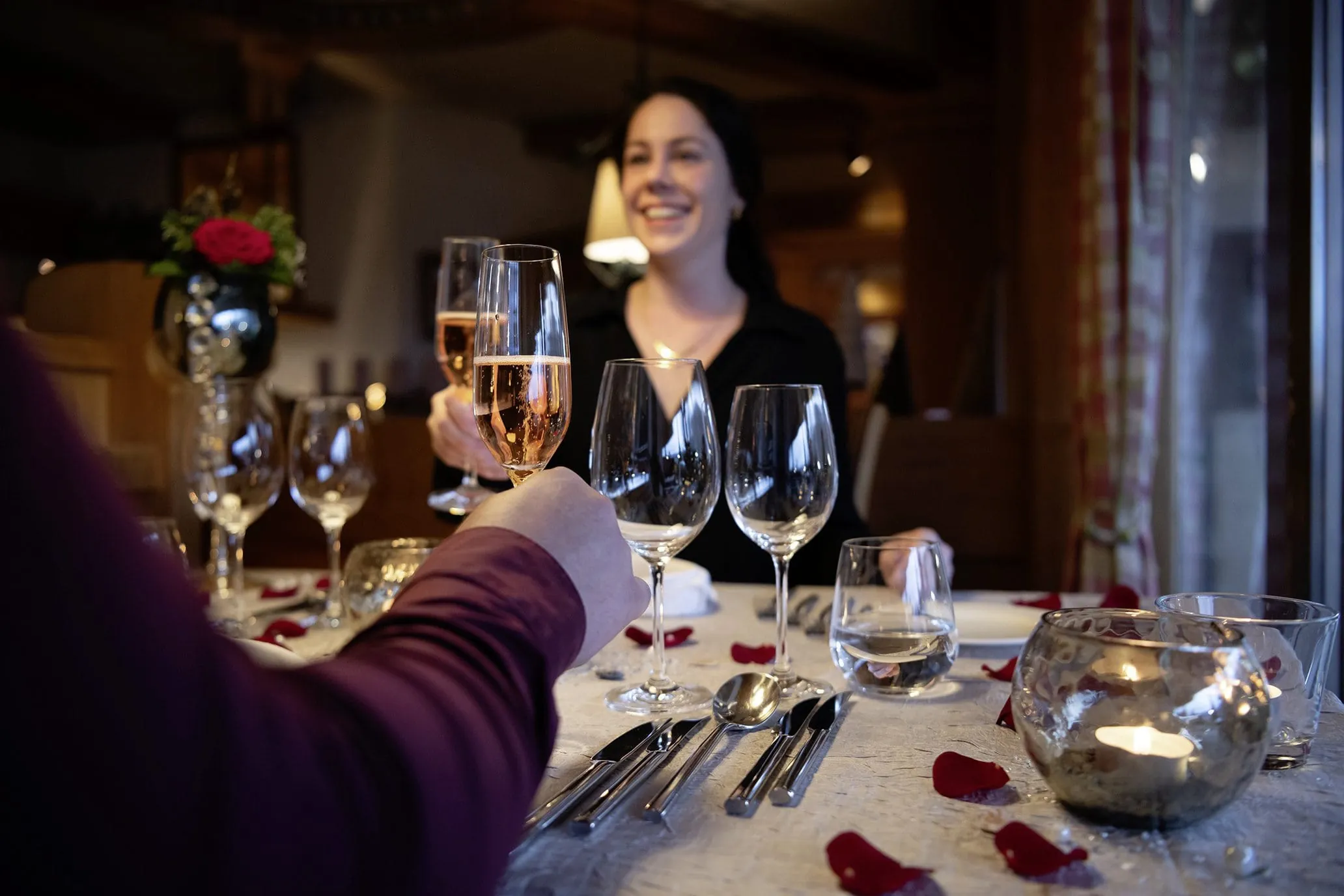 Paar an Restauranttisch im Salzano mit Rosenbl&auml;ttern prostet sich mit Sekt zu