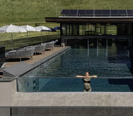 Frau in schwarzem Bikini steht am Panoramafenster des Outdoorpool im Terentnerhof