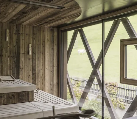 Sauna im Terentnerhof mit Holzbalken vor dem Fenster und Blick auf die Wiese