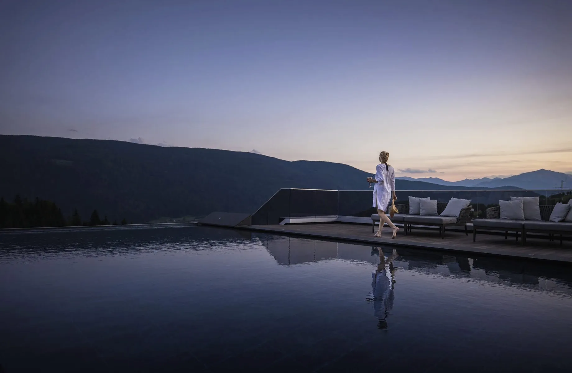 Frau in weißem Kleid am Beckenrand des Außenpools im Terentnerhof im Sonnenuntergang