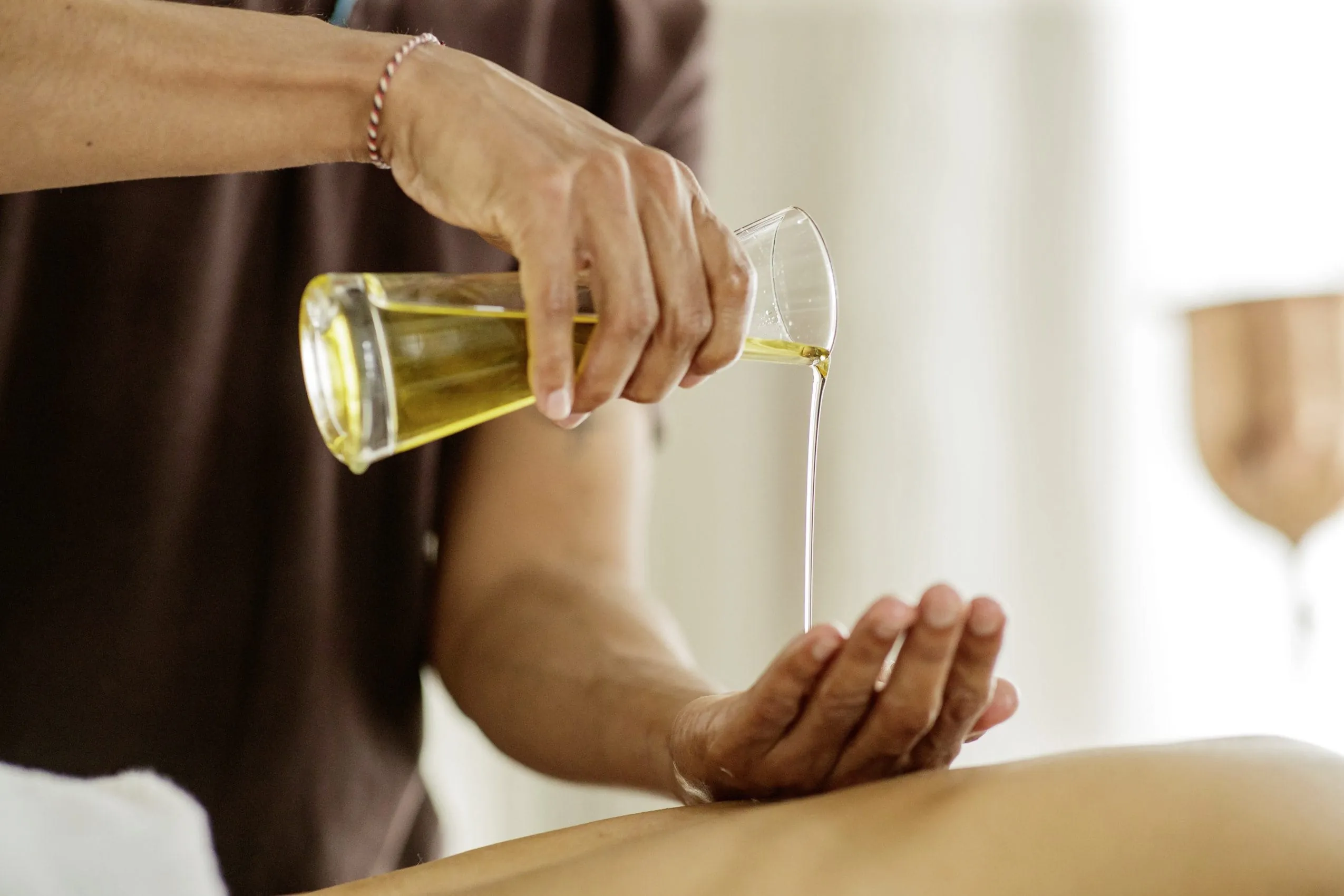 Masseur gie&szlig;t aus Glaskaraffe &Ouml;l auf seine Hand im Posthotel Achenkirch