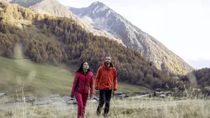 Ein Mann und eine Frau gehen auf einem Wanderweg in den Bergen in der Nähe der Südtirol Chalets Valsegg, umgeben von herbstlich gefärbten Bäumen und einer Berglandschaft