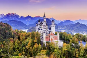 Blick auf Schloss Neuschwanstein vor bayerischer Alpenkulisse und untergehender Sonne im Herbst