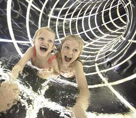 Zwei Mädchen in Badesachen in einer Rutsche des Familotel Allgäuer Berghof mit spiralförmigen Lichtern