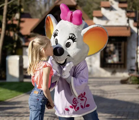 Mädchen küsst das Maskottchen Edda Euromaus mit großen Ohren und einer rosa Schleife im Erlebnishotel Colosseo