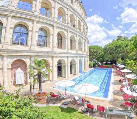 Fassade des Erlebnishotels Colosseo mit Kolosseum Nachbildung, langem Outdoorpool und roten Liegen