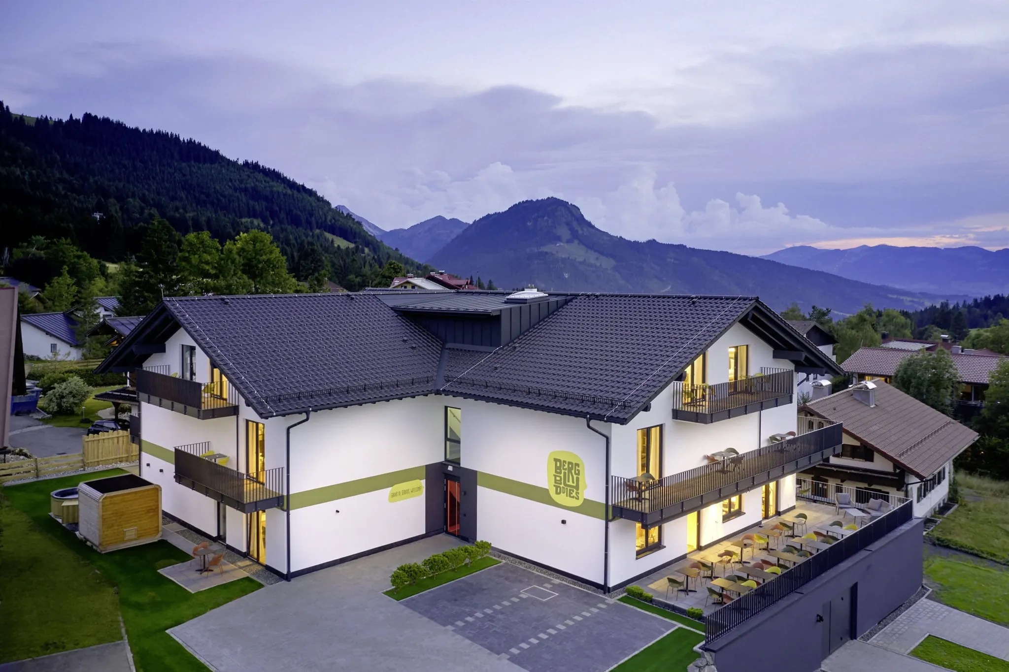 Blick aus der Vogelperspektive auf das BergBuddies-Hotel im Sommer, im Hintergrund die Berge