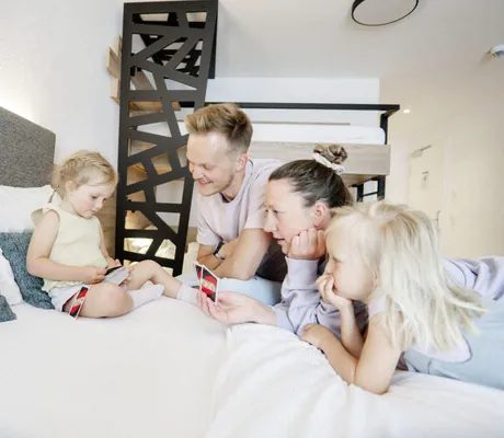 Junge Familien mit zwei Kindern liegt auf dem Bett und spielt Uno