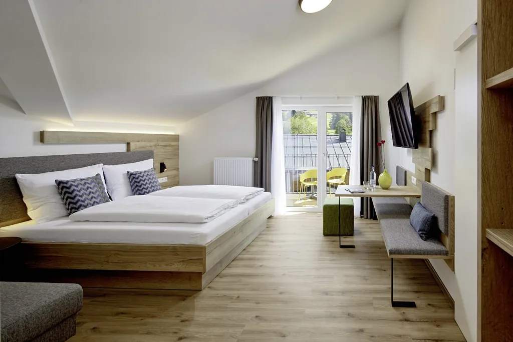 Blick in ein modernes Zimmer mit Doppelbett, Ess- und Sitzmöglichkeit und Balkon