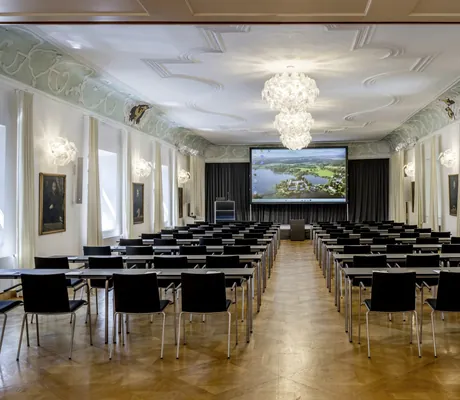großer Festsaal im Kloster Seeon mit schwarzen Stühlen, Stuckdecke und weißen Kronleuchtern