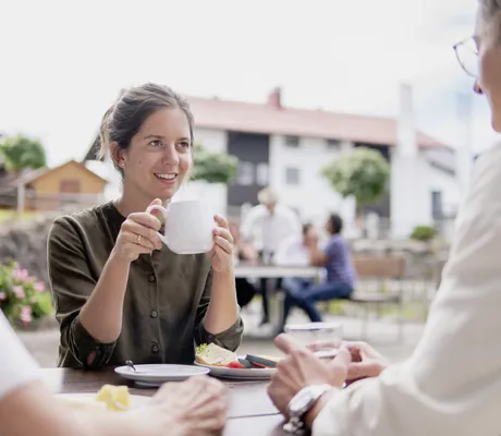 Frau in olivfarbener Bluse trinkt Kaffee in der Gruppe am Outdoortisch im Panoramahotel Oberjoch