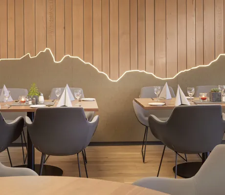 eingedeckte Tische im Restaurant des Westerham - die Akademie mit stilisierter Bergkulisse an der Holzwand