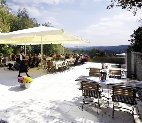 große Terrasse mit Bestuhlung unter großen weißen Sonnenschirmen und bewirteter Gruppe im Westerham - die Akademie
