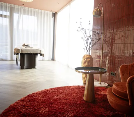 Heller Behandlungsraum mit roten Farbakzenten und bodentiefen Fenstern