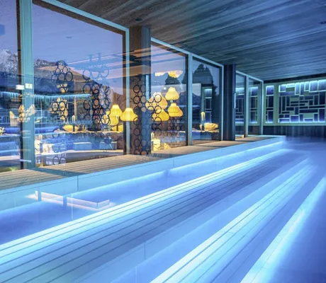 Stimmungsvoll in Blau-Tönen beleuchtete Sauna mit großen Fenstern mit Blick Richtung Alpen