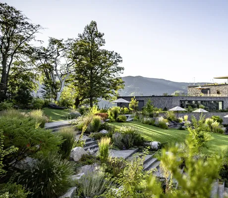 Naturgarten mit weißen Sonnenschirmen vor der verschindelten Fassade des Luisenhöhe Gesundheitsresort