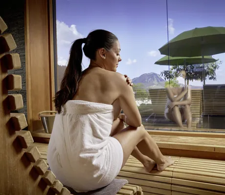 dunkelhaarige Frau mit Zopf sitzt in der Sauna des Panoramahotel Oberjoch am Fenster