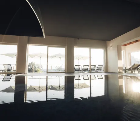 spiegelglatter Indoorpool im Thula Wellnesshotel mit Blick auf die Liegestühle vor dem Panoramafenster