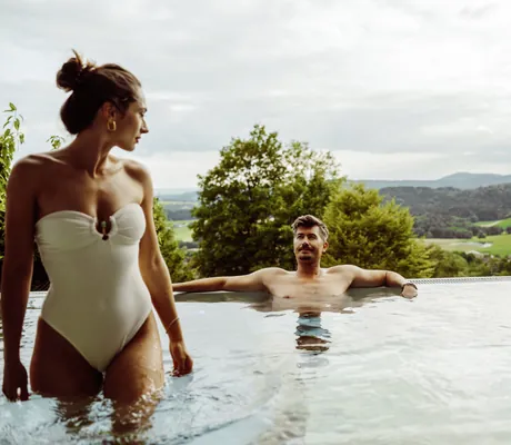 Frau in weißem Badeanzug verlässt den Outdoorpool in dem der Mann liegt in Thula Wellnesshotel