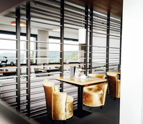 goldene Sessel an Holztisch im Restaurant vor Lamellenwand in Thula Wellnesshotel
