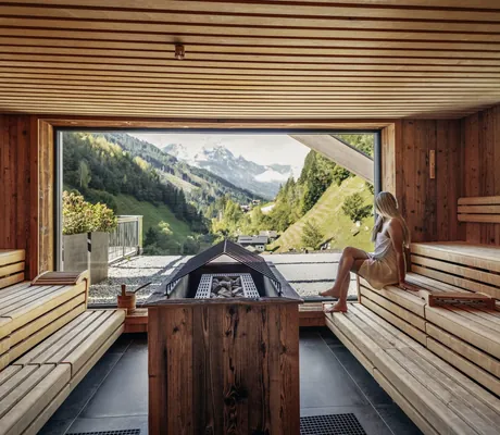 blonde Frau sitzt in der Sauna des ZillergrundRock und blickt in das idyllische Zillertal