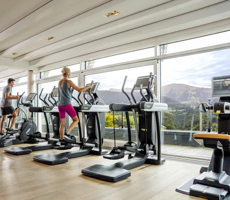 Mann und Frau auf Steppern im Fitnessraum des Hotel Allgäu Sonne mit Blick in die Berge