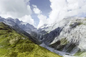 Berglandschaft mit grünen Hängen links und steilen, felsigen Hängen rechts unter bewölktem Himmel in der Nähe des Hotel Mischun