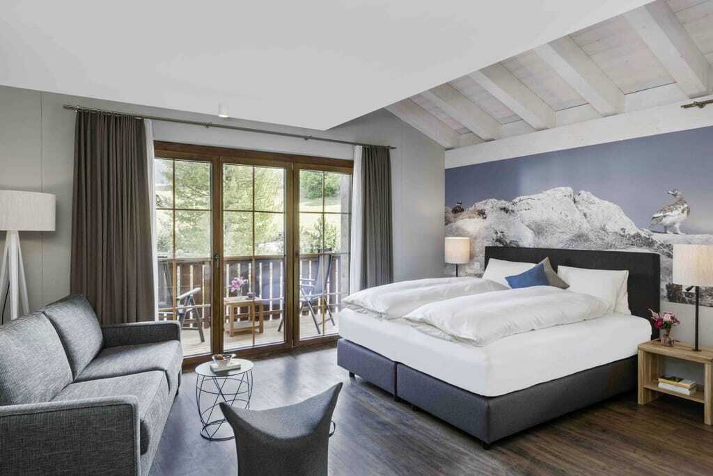 Juniorsuite im Hotel Mischun mit großem Bett, grauem Sofa, Holzboden und Balkon mit Blick ins Grüne