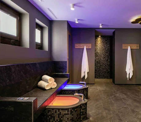 Moderner Wellnessbereich im Hotel Mischun mit zwei Fußbädern, Handtüchern an Haken und indirekter Beleuchtung in warmen Farben