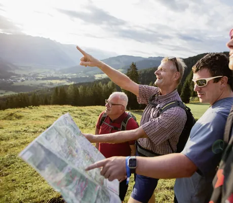 vier Menschen in Wanderoutfit schauen bei einer Wanderung auf eine Karte in der Nähe der Riederalm