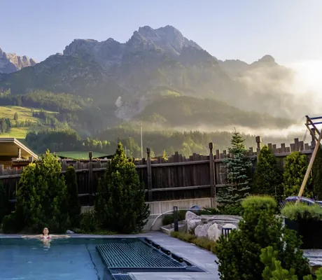 Frau liegt am Beckenrand des Outdoorpools der Riederalm und schaut in den Himmel