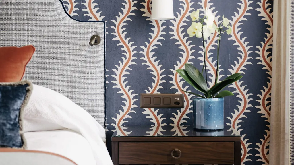 Detail am Bett im Zimmer des Suvretta House mit blau-gemusterter Tapete und Orchidee