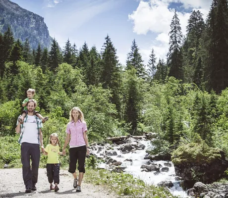 Familien mit zwei Kindern wandert Hand in Hand an einem Bach entlang rund um das Wanderhotel Gassner