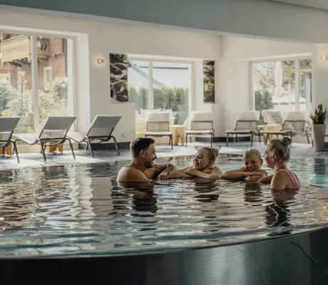 Familie lehnt am Beckenrand des Indoorpools im Wanderhotel Gassner