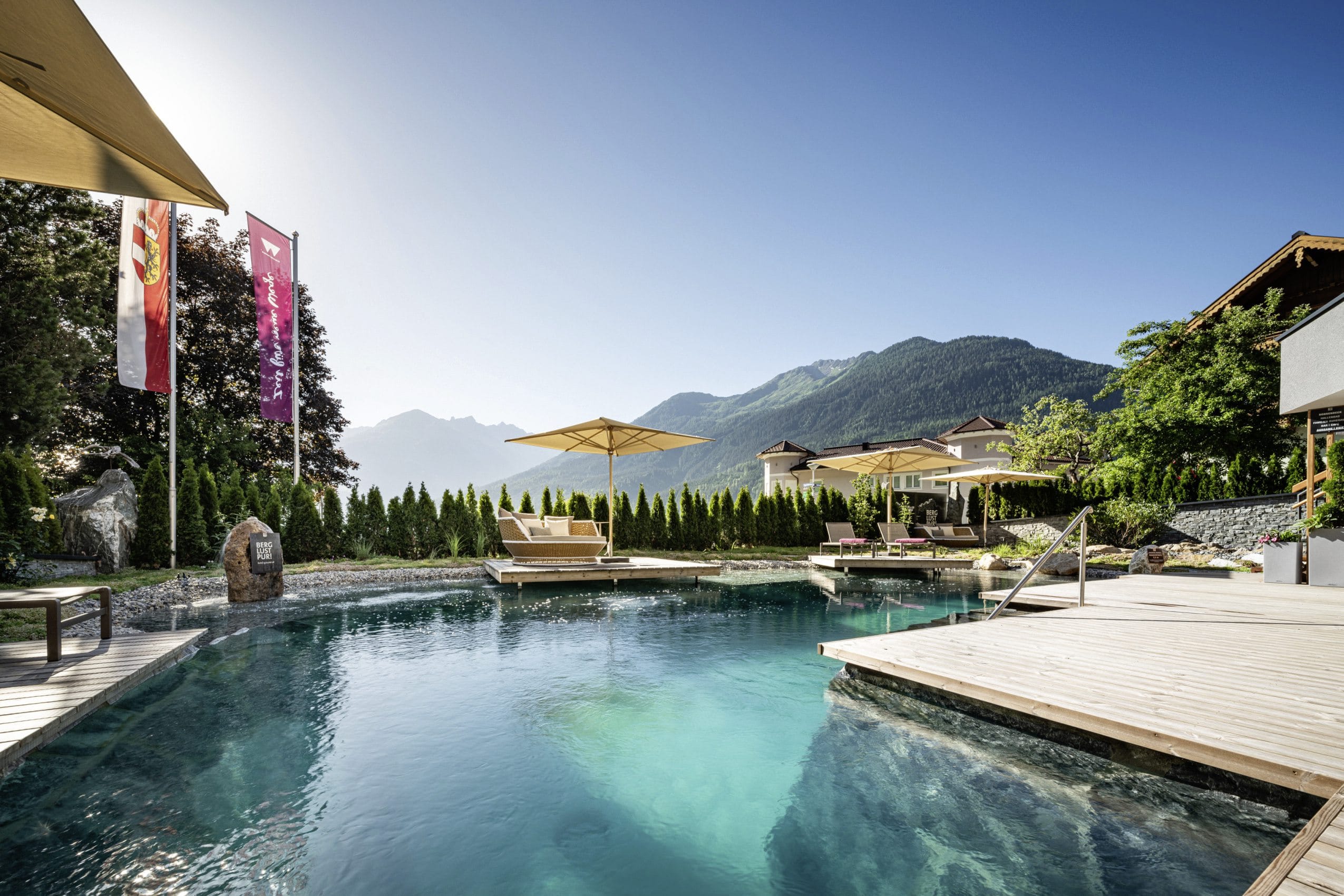 Naturpool im Wanderhotel Gassner mit Holzsteg und gehissten Flaggen