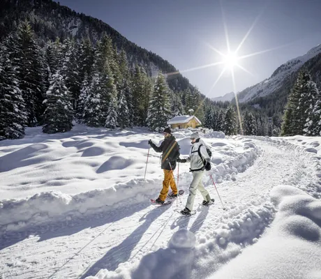 Paar im Winteroutfit wandert mit Schneeschuhen auf einem verschneiten Weg am Wanderhotel Gassner